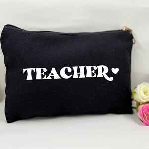 May include: Black canvas zippered pouch with white text that reads "TEACHER" and a small white heart.