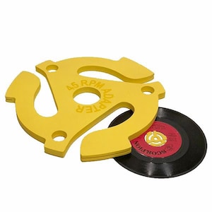 May include: A yellow 45 RPM adapter with the text "45 RPM ADAPTER" and a black vinyl record with red and white labels. The adapter is designed to fit over the center hole of a 7-inch record.