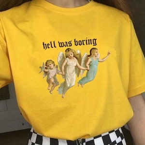 May include: Yellow t-shirt with a graphic of three angels and the text "hell was boring" printed in black.