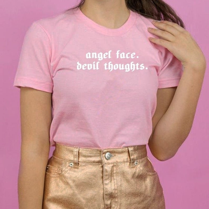 May include: A pink t-shirt with the text "angel face. devil thoughts." in white lettering.