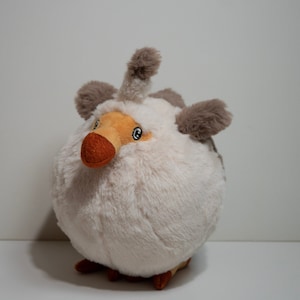 Pode incluir: Um brinquedo de pelúcia em forma de pássaro com um corpo redondo e macio pelo branco. Possui detalhes marrons nas orelhas e na cabeça, um bico marrom e pequenos olhos azuis. O brinquedo é projetado para se assemelhar a um pássaro.