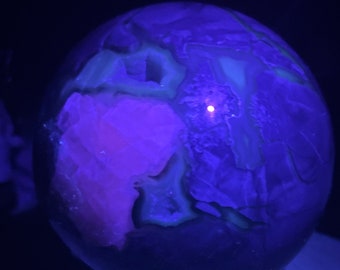 May include: A large, purple and green crystal sphere with a white light shining through it. The sphere is sitting on a wooden base.