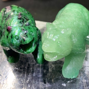 May include: Two green stone carvings of bears. One bear is a darker green with black and pink flecks, the other is a lighter green.