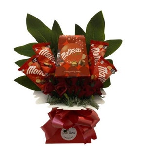 Puede incluir: Una caja roja y blanca de chocolates Maltesers rodeada de rosas rojas y hojas verdes en una caja de regalo roja y blanca. La caja dice "Maltesers" y "Crunchy Chocolate Treats".