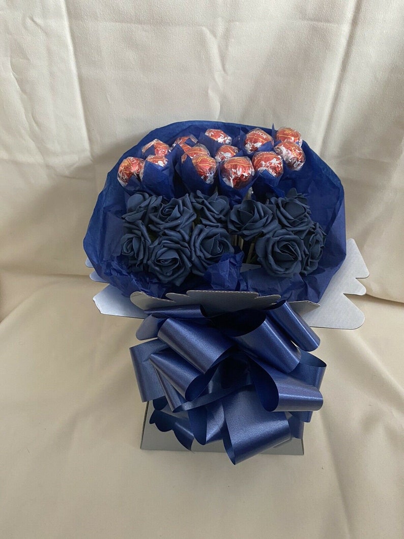 Puede incluir: Un ramo de rosas artificiales azules con una cinta azul y un centro de caramelos de chocolate envueltos en papel de aluminio rojo.