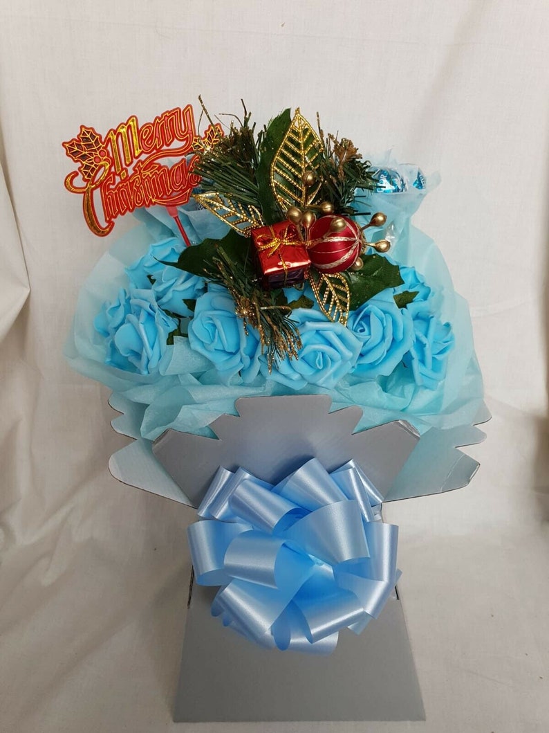 May include: A blue and silver Christmas bouquet with a blue bow, a red gift box, and a gold ornament. The bouquet has a "Merry Christmas" sign on top.