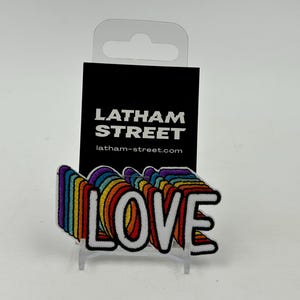 May include: Rainbow-coloured "LOVE" patch with a white background. The patch is attached to a card with the text "LATHAM STREET" and the website address "latham-street.com".