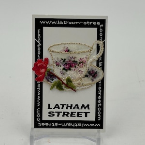 May include: A white teacup and saucer with a floral pattern and gold trim. A red rose with green leaves is next to the teacup. The text "LATHAM STREET" is printed below the teacup. The text "www.latham-street.com" is printed around the border of the card.