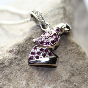 May include: A silver pendant necklace with a dove design. The dove is encrusted with small purple and white gemstones.