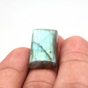 May include: A rectangular, iridescent green labradorite gemstone with a smooth, polished surface.