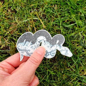 以下が含まれることがあります： 蛇の体に山脈と星空が描かれた白黒のステッカーです。