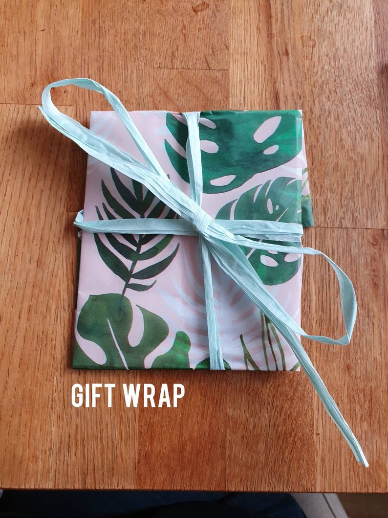May include: A gift wrapped in pink and green tropical leaf patterned paper with a light blue ribbon tied in a bow. The text "GIFT WRAP" is printed on the bottom of the image.