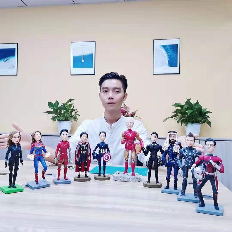 May include: A collection of superhero figurines, including Iron Man, Captain America, Black Widow, and Thor. The figurines are made of painted resin and are approximately 10 inches tall. The figurines are displayed on a table in front of a man.