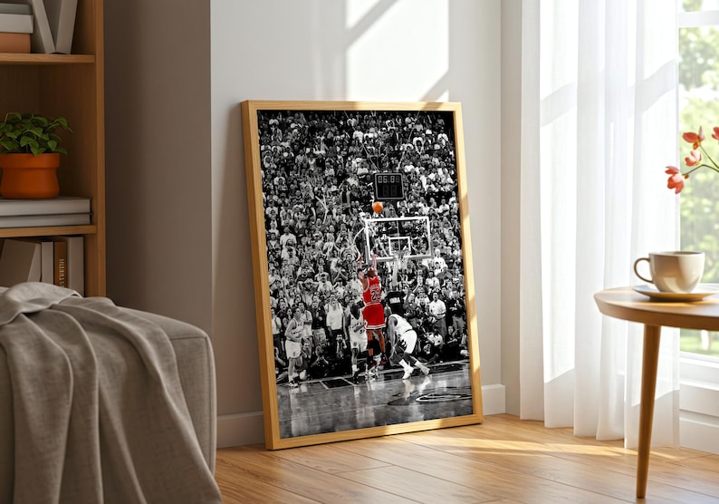May include: A framed vertical wall art print featuring a black and white photograph of a basketball game in progress. A player in a red jersey is jumping to shoot an orange basketball toward a hoop, surrounded by a large crowd of spectators.