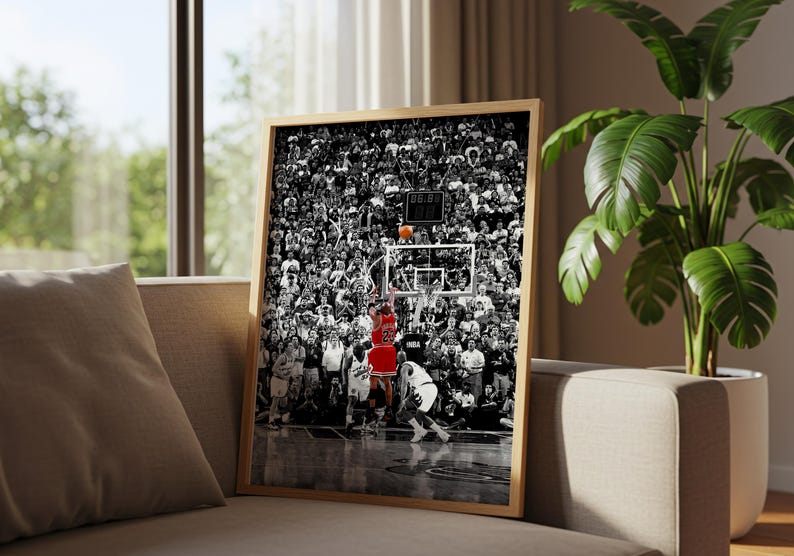 May include: A framed vertical wall art print featuring a black and white photograph of a crowded basketball arena. A single player in a red jersey is jumping to shoot an orange basketball toward the hoop, standing out against the monochrome crowd.