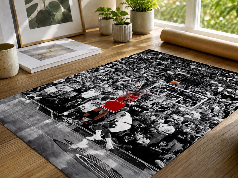 May include: A rectangular poster featuring a black and white photograph of a basketball game in progress. A player in a red jersey with the number 23 is captured mid-air near the hoop, while the surrounding crowd is rendered in monochrome.
