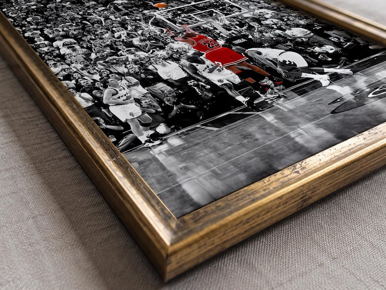 May include: A framed wall art print featuring a black and white photograph of a basketball game with a crowd in the background. A player in a red jersey is jumping toward the hoop. The frame is made of dark, distressed wood with gold tones.