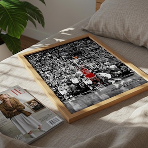May include: A rectangular wooden frame containing a black and white photograph of a basketball game. The image features a player in a red jersey with the number 23, surrounded by a crowd of spectators and players on a basketball court.