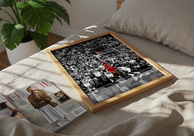 May include: A rectangular wooden frame containing a black and white photograph of a basketball game. The image features a player in a red jersey with the number 23, surrounded by a crowd of spectators and players on a basketball court.
