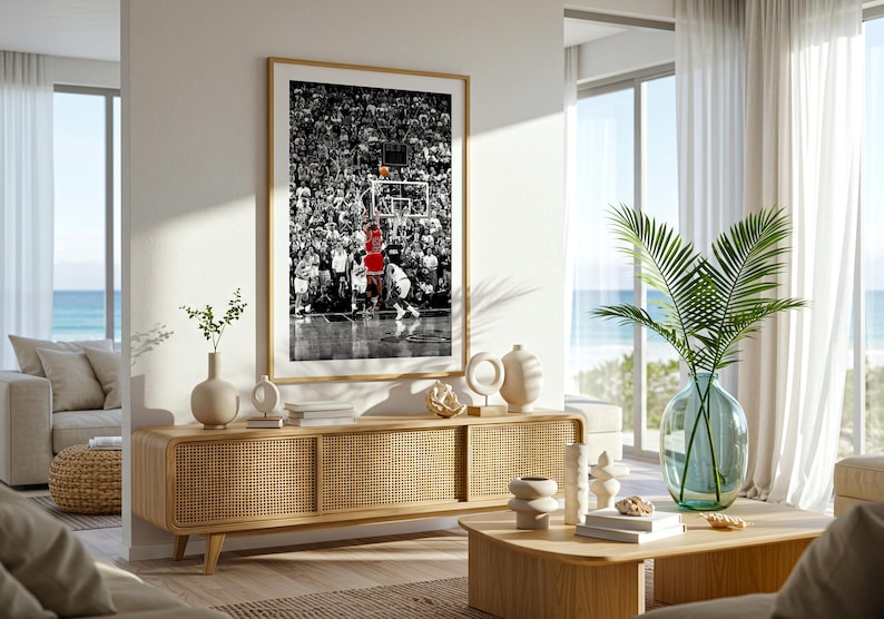 May include: A framed vertical wall art print featuring a black and white photograph of a basketball game with a player in a red jersey shooting a basketball toward the hoop, displayed above a light wood media console with cane cabinet doors.