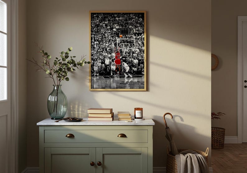 May include: A framed rectangular wall art print featuring a black and white photograph of a basketball game with a player in a red jersey jumping toward the hoop. The print is displayed in a thin light wood frame hanging on a neutral wall.