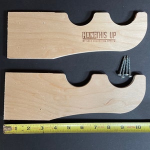 K&ouml;nnte beinhalten: Zwei unfertige Holzregalb&ouml;cke mit drei Aussparungen zum Aufh&auml;ngen von Gegenst&auml;nden. Die B&ouml;cke sind 17,8 cm lang und haben vorgebohrte L&ouml;cher zur Montage. Der Text "HANGTHIS UP MY SHED ORGANIZING SYSTEM" ist in den oberen Bock graviert.