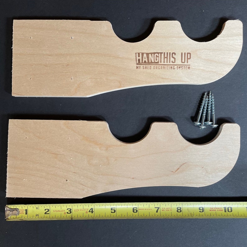 K&ouml;nnte beinhalten: Zwei unfertige Holzregalb&ouml;cke mit drei Aussparungen zum Aufh&auml;ngen von Gegenst&auml;nden. Die B&ouml;cke sind 17,8 cm lang und haben vorgebohrte L&ouml;cher zur Montage. Der Text "HANGTHIS UP MY SHED ORGANIZING SYSTEM" ist in den oberen Bock graviert.