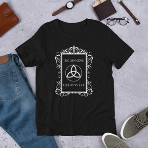 May include: Black t-shirt with a white graphic design featuring a stylized symbol with the text "SIC MVNDVS CREATVS EST" in a decorative frame.