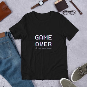 May include: Black t-shirt with a pixelated "GAME OVER" graphic in white and blue. The text "Press start to continue" is below the graphic.