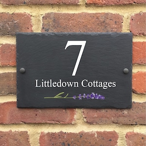 May include: Black slate house number sign with white lettering. The number 7 and the text "Littledown Cottages" are displayed on the sign. A small lavender sprig is depicted below the text.