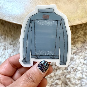 May include: A blue denim jacket sticker with white floral embroidery on the back. The sticker has a brown leather patch with the word "Levi's" on it.