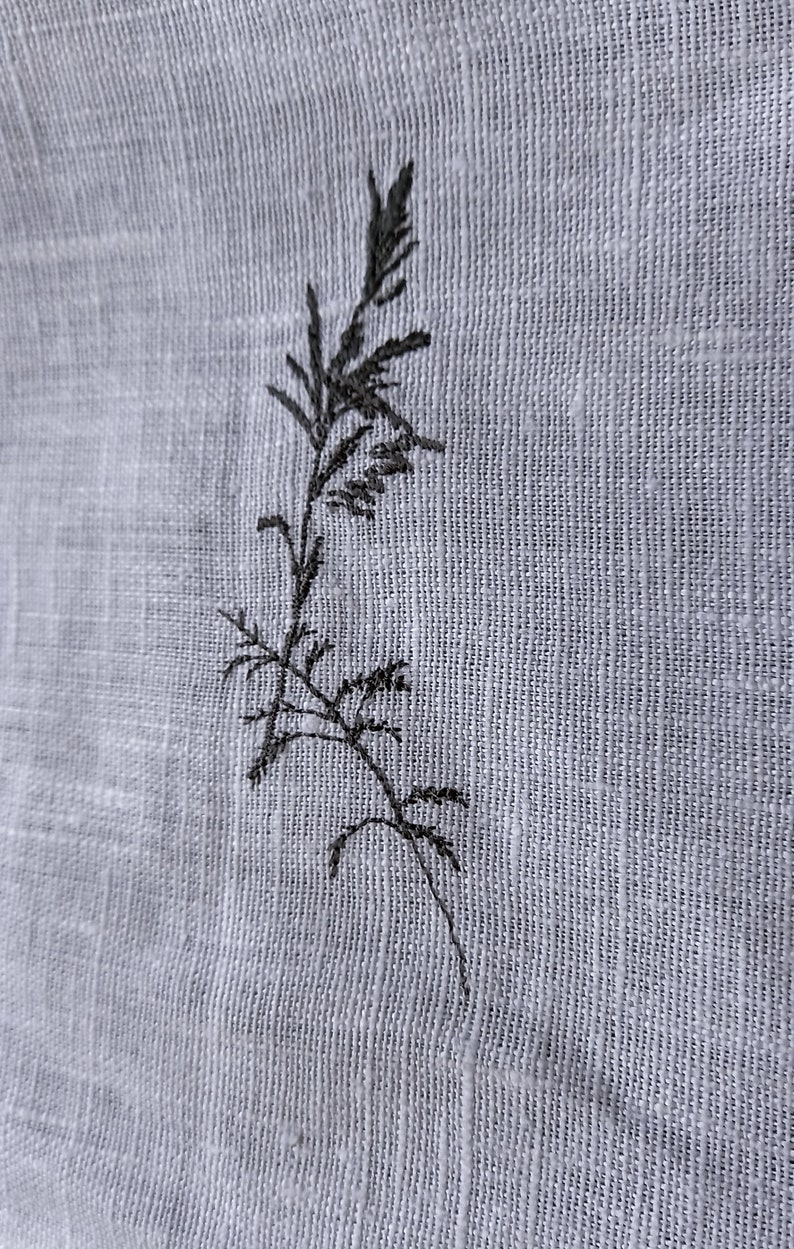 May include: A black embroidered design of a single plant stem with leaves on a white fabric background.