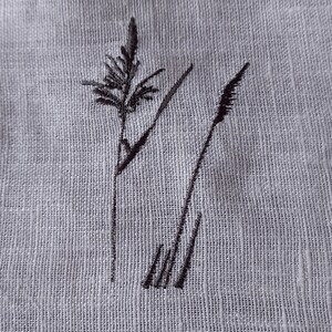 May include: Black embroidered design of two tall grass stalks on a white linen fabric.