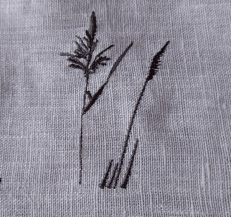 May include: Black embroidered design of two tall grass stalks on a white linen fabric.