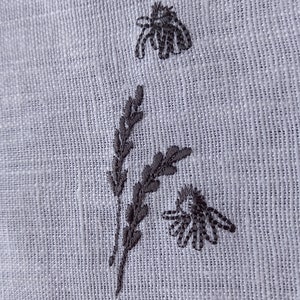 May include: Embroidered design on a white fabric featuring two stylized bees and a sprig of leaves.