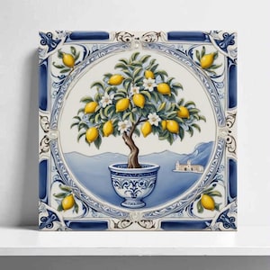 May include: Square ceramic tile depicting a lemon tree in a decorative pot. The tree bears yellow lemons and white blossoms, set against a blue and white backdrop with a coastal scene. The tile has a detailed border.