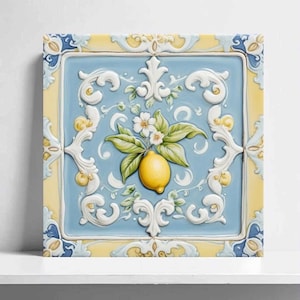 Könnte beinhalten: Quadratische Keramikfliese mit Zitronenmotiv. Die Fliese zeigt eine gelbe Zitrone mit grünen Blättern und weißen Blüten auf hellblauem Hintergrund. Der Rand ist gelb und blau mit weißen Schnörkeln.