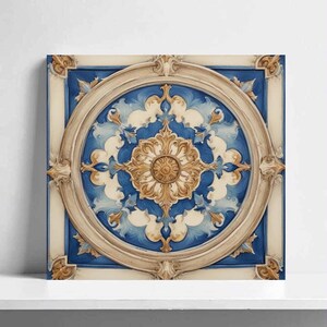 May include: Square wall art featuring a detailed, ornate design. The artwork showcases a central circular motif with a gold and cream-colored floral pattern against a blue and white background. The piece is framed with a cream-colored border and decorative accents.