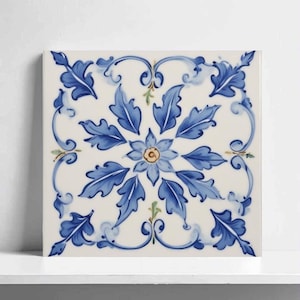 May include: Square ceramic tile with a floral design. The tile features a central flower with blue petals and a yellow centre, surrounded by blue leaves and decorative swirls on a white background.