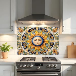 May include: A decorative kitchen splashback featuring a sun design with a face in the centre. The sun is surrounded by a blue and yellow floral pattern. The splashback is installed above a stainless steel cooker.
