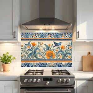 May include: Kitchen backsplash tile with a floral and bird design. The tile has a cream background with blue, orange, and green floral patterns. A blue bird is perched on a branch. The tile is installed above a stainless steel cooker.