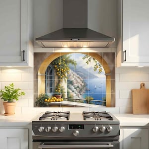 May include: A kitchen backsplash featuring a scenic Italian coastal view with a yellow archway, lemons, and a blue sea. The artwork is installed above a stainless steel gas range and between white cabinets.