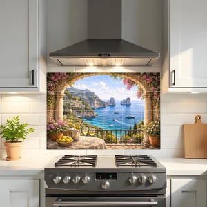 May include: A kitchen backsplash mural featuring a coastal Mediterranean scene with a stone archway, pink flowers, a table with lemons and wine glasses, and a view of the sea with rock formations, installed between white cabinets and a stove.