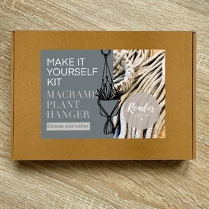May include: A brown cardboard box with a grey label that says "Make it Yourself Kit Macrame Plant Hanger Choose your colour" and a picture of a macrame plant hanger. The label also has the text "Rondlos Creations" on it.