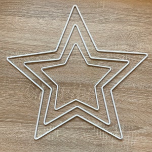 May include: Three nested white metal star shapes. The stars are arranged in a layered design, with each star slightly smaller than the one surrounding it. The stars are made of thin metal wire and are painted white.