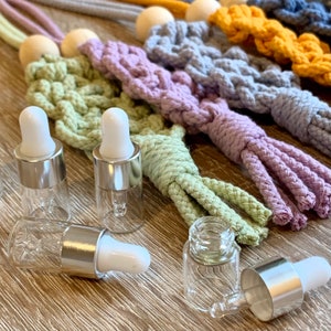 May include: Five clear glass bottles with silver tops and droppers. The bottles are arranged on a wooden surface with colourful crocheted tassels in the background.