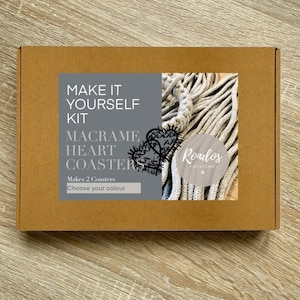 May include: A brown cardboard box with a label that says "Make It Yourself Kit Macrame Heart Coasters" and "Makes 2 Coasters Choose your colour". The label also features a drawing of two cactus plants with hearts. The box contains a kit to make macrame heart coasters.