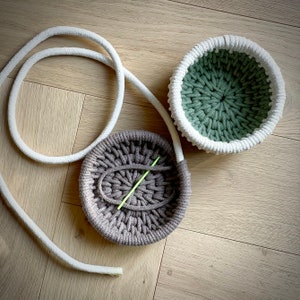 May include: Two crocheted bowls, one green and one brown, with a white rope cord. The brown bowl has a green crochet needle inside.
