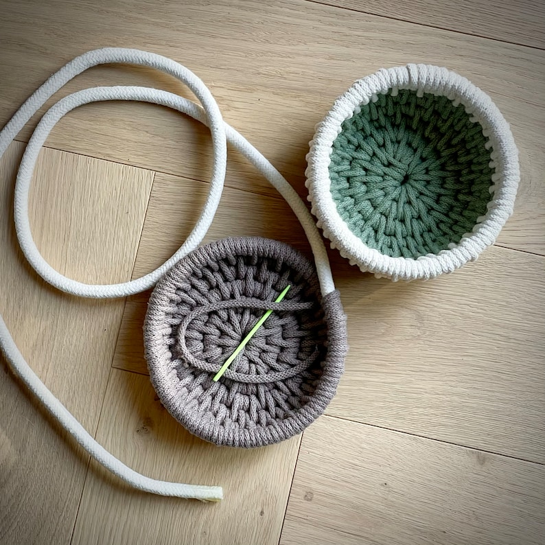 May include: Two crocheted bowls, one green and one brown, with a white rope cord. The brown bowl has a green crochet needle inside.