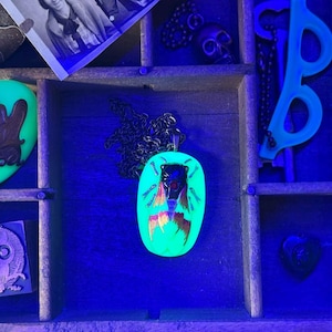 May include: A collection of spooky-themed items, including a glowing green pendant with a bug design, a skull, and a stamp with an owl design. The items are displayed in a wooden organizer.